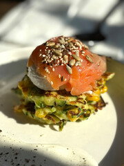Zucchini and Corn Pancakes with Poached Egg, Lightly Salted Fish, Flax Seeds, Sunflower Seeds, and Sesame. Healthy Cafе Breakfast Concept. Handmade Mobile Photo, Harsh Sunlight, Selective Focus, Non-A