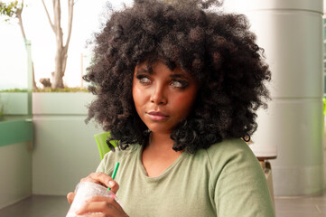A Young Woman with Beautiful Curly Hair Enjoying a Refreshing Beverage While Indoors