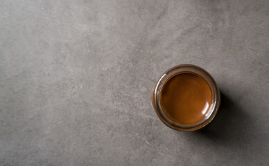 Top view of chocolate spread or nougat cream with hazelnuts in glass jar on dark background