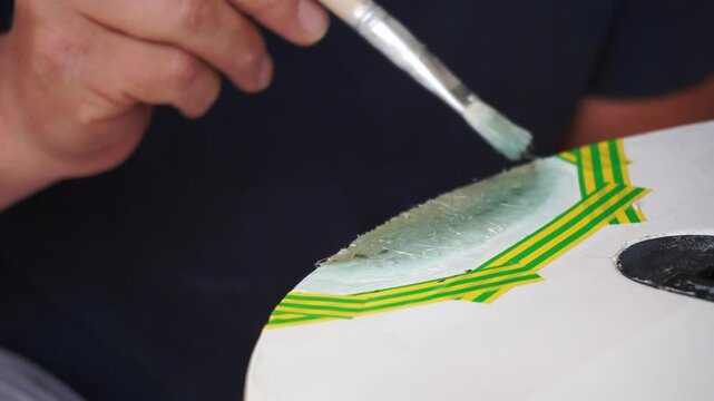 Man applies an epoxy patch repairing windsurfing board