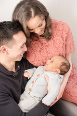 Parents smile down at baby as they cradle them together with love