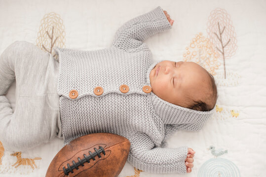 Newborn baby napping with football on woodland-themed blanket