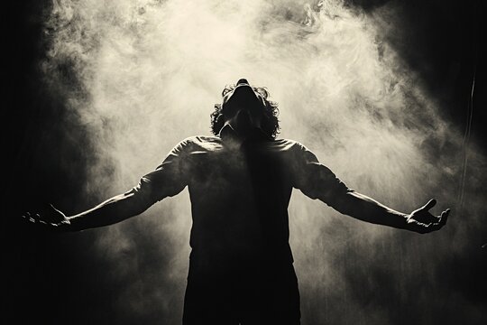 Young man opened his arms, worshiping god on smoky background.