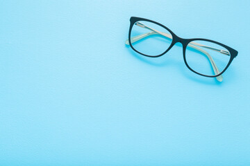 Eyeglasses with dark black plastic frame on light blue table background. Pastel color. Closeup. Empty place for text. Top down view.