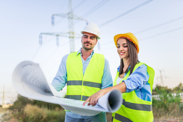 Electrical engineers discussing project using blueprints near power lines