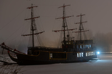 An ancient frigate frozen in ice stands at the pier on a winter evening