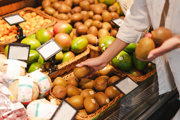 Woman choosing fresh kiwi fruits in supermarket grocery store closeup, selective focus
