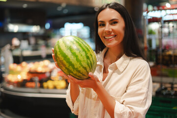 Fototapeta premium Attractive, happy smiling Latin woman holding watermelon in supermarket