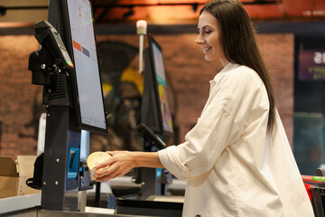 Customer using self-checkout kiosk scanning groceries in supermarket