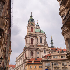 Fototapeta premium Baroque Church of St. Nicholas in Prague’s Lesser Town, framed by ornate historical buildings under a cloudy sky.