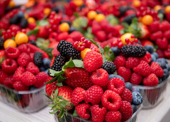 Fresh mixed berries in market trays including strawberries, raspberries, blueberries, blackberries, redcurrants and physalis, vibrant and ready to eat, ideal for healthy food concepts.