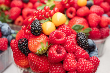 Close-up of fresh berry mix with raspberries, strawberries, blackberries, redcurrants, blueberries, and golden physalis in a transparent container, ideal for healthy food and summer fruit themes.