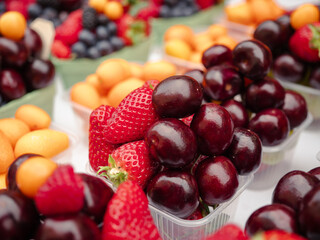 Fresh cherries, strawberries, physalis and raspberries arranged in plastic trays at a fruit market, vibrant and juicy, ideal for healthy food and summer produce themes.

