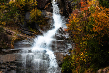 Autumn Waterfall Cascading Over Rocky Cliff in Forested Mountain Valley