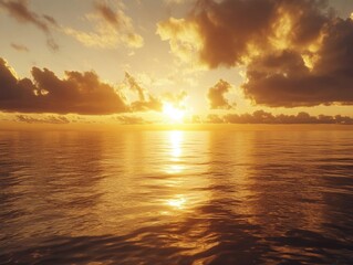 Fototapeta premium Picture of a tranquil ocean at sunset with golden light reflecting on the water, under a sky filled with clouds.