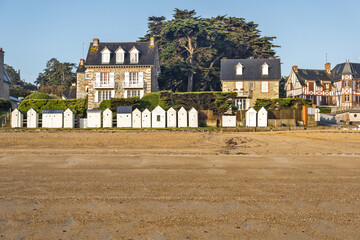 A beach at low tide with wet sand that reflects the buildings with traditional architecture  A row of beach huts typical of seaside resorts at Saint-Cast-Le-Guildo in Brittany, France