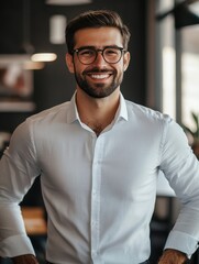 Young professional with beard, glasses and white shirt standing confidently in modern office environment.