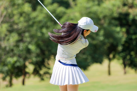  Asian woman happy and fun while playing golf on the golf course. Golfer hitting golf shot with driver club on course. Beautiful woman smiling and holding a golf club while standing on green lawn.