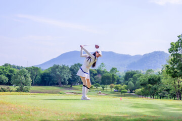  Asian woman happy and fun while playing golf on the golf course. Golfer hitting golf shot with driver club on course. Beautiful woman smiling and holding a golf club while standing on green lawn.