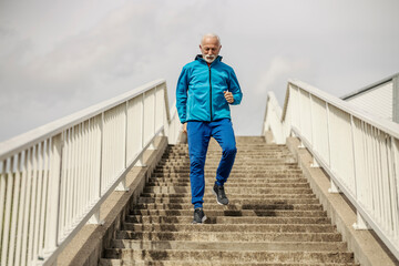 Full length of an old athlete running down the stairs on a bridge.