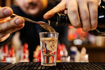 Close up of bartender's hand adding liqueur into a cocktail shot and making monkey brain cocktail.