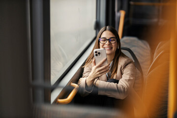 Portrait of a happy woman riding public city bus and smiling at cellphone.