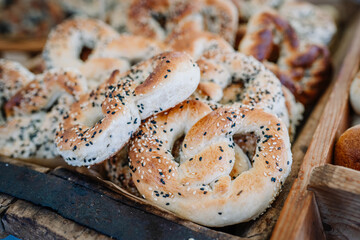 Close-up of freshly baked sesame pretzels with golden crust and seed toppings, arranged in a bakery or market setting. Rustic and appetizing detail..