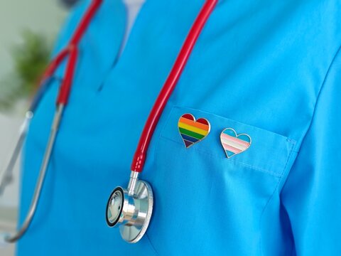 Woman doctor shows lgbt pride flag in her hand in hospital office. Medical support for lgbt community and symbol of tolerance concept