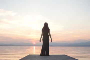 woman in black contemplates the sea at sunset from the pier