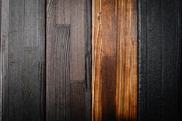 Close-up of vertically arranged burnt wooden planks in various shades from light brown to deep...