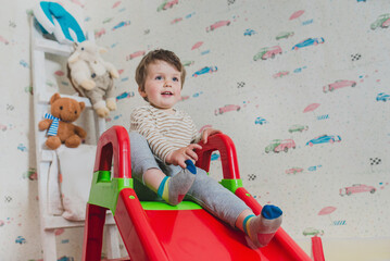 Fototapeta premium Baby slides down a slide, games in the nursery. Carefree childhood, children's centers and attractions. Choosing a nanny, safe leisure for children