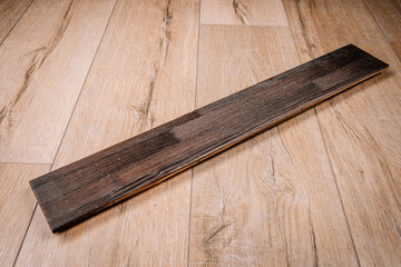 Charred wooden plank with dark finish placed on a light wood floor. Close-up showcasing texture and contrast. Burnt wood style. Suitable for design use..