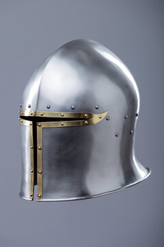 Silver Medieval Barbute Helmet with Brass Trim. This image shows a shiny silver helmet with a distinctive T-shaped opening for the face, accented with brass trim and rivets.