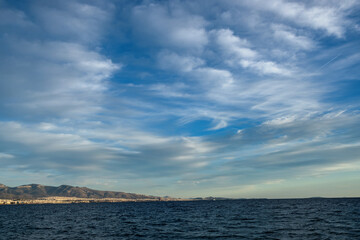Pattern of fluffy and feathery white clouds in the bright blue sky over the Gulf of Athens