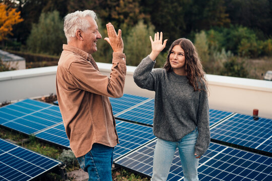 Grandfather and granddaughter high-fiving near solar panels outdoors