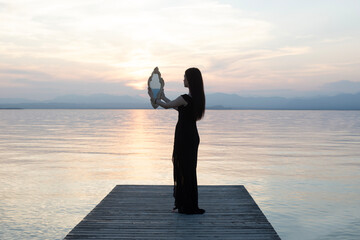 Woman in black dress with mirror in front of the sea: reflections between reality and introspection
