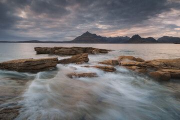 Obraz premium Dramatic waves crash against Elgol’s rugged coast, with the Cuillin Mountains rising in the misty distance. Autumn’s golden light enhances this wild, untamed beauty.