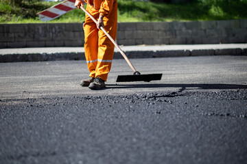Road construction worker smooths asphalt during repairs in a busy urban area on a sunny day