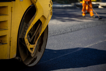 Road construction work in progress with a yellow roller and worker smoothing asphalt