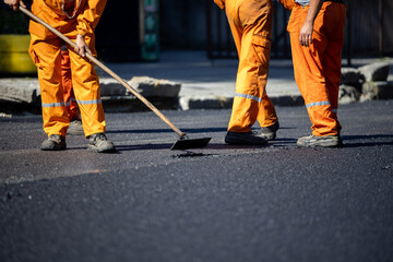 Construction workers repair asphalt road in bright orange uniforms during daytime