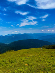 Fototapeta premium Traveler hiking in the mountains of Adjara, Georgia, with a wide view of massive peaks, Alpine meadows, green grass, and wildflowers. Concept of travel, adventure, and eco tourism in Europe
