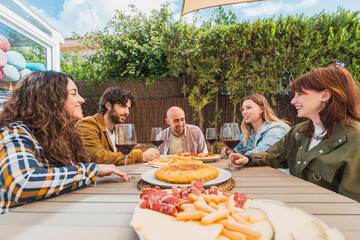 Friends Sharing Food and Wine at Outdoor Lunch Gathering - Group of friends enjoying conversation over wine and traditional food at an outdoor lunch table - Food and beverage concept with friends