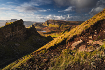 Autumn light bathes the Quiraing on Skye, casting long shadows over its dramatic cliffs and rolling hills. The landscape glows with golden hues, a breathtaking Highland scene.