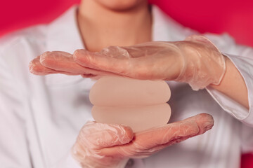 Naklejka premium Close-up of a woman hands in transparent gloves holding silicone round breast implants. The hands of a female surgeon with modern thoracic endoprostheses.