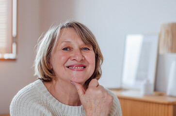 Close-up portrait of an elderly woman in a sweater. A beautiful middle-aged lady in casual clothes is smiling in the living room. A pensioner poses at home.