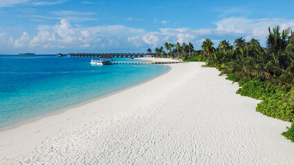 Aerial view of the beautiful tropical landscape on the islands. A clean deserted sandy beach and palm trees. Blue ocean water and a marina with a boat.