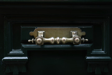 Horizontal metal patterned handle on the dark green entrance door. Close-up