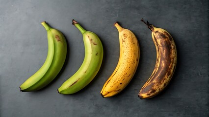 Four bananas ripening stages green yellow brown over dark background