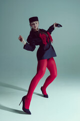 Young woman in black jacket, red fringed details, red tights, and heels striking dynamic pose,...