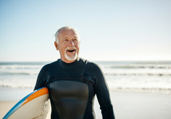 Elderly man in wetsuit holding surfboard on sunny beach day